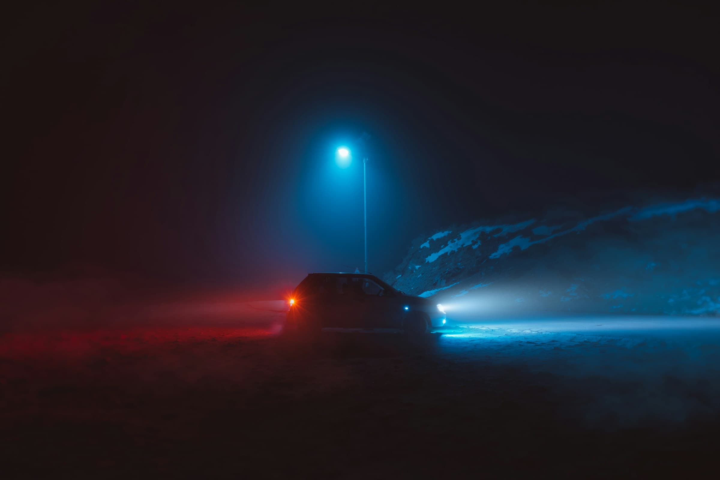 Modern car at night with headlights cutting through fog on an open road